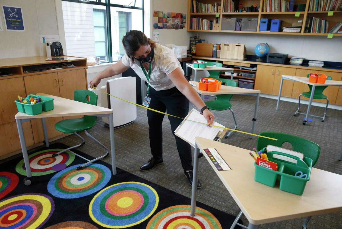 Gianna Fazioli, a safety inspector with the city, measures the distance between desks in a classroom during a tour of the San Francisco School before authorizing in-person learning on the campus in San Francisco on Sept. 17. The private school with 285 students enrolled was among the first schools in the city to apply for in-classroom instruction last year during the coronavirus pandemic.