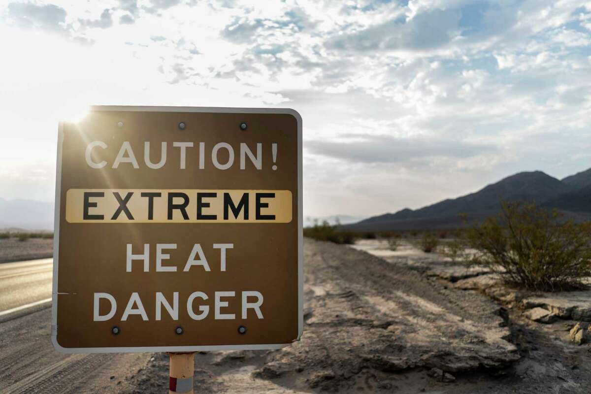 With the Amargosa Mountain Range in the background at sunrise, a sign warns park visitors of "extreme heat danger" along Highway 190 on Sunday.