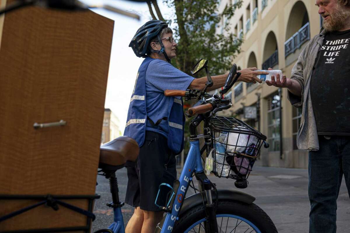 Sister Libby Fernandez, executive director with Mercy Pedalers, left, hands a bottle of water to a person experiencing homelessness during a heatwave in Sacramento, Calif., on July 8, 2021.