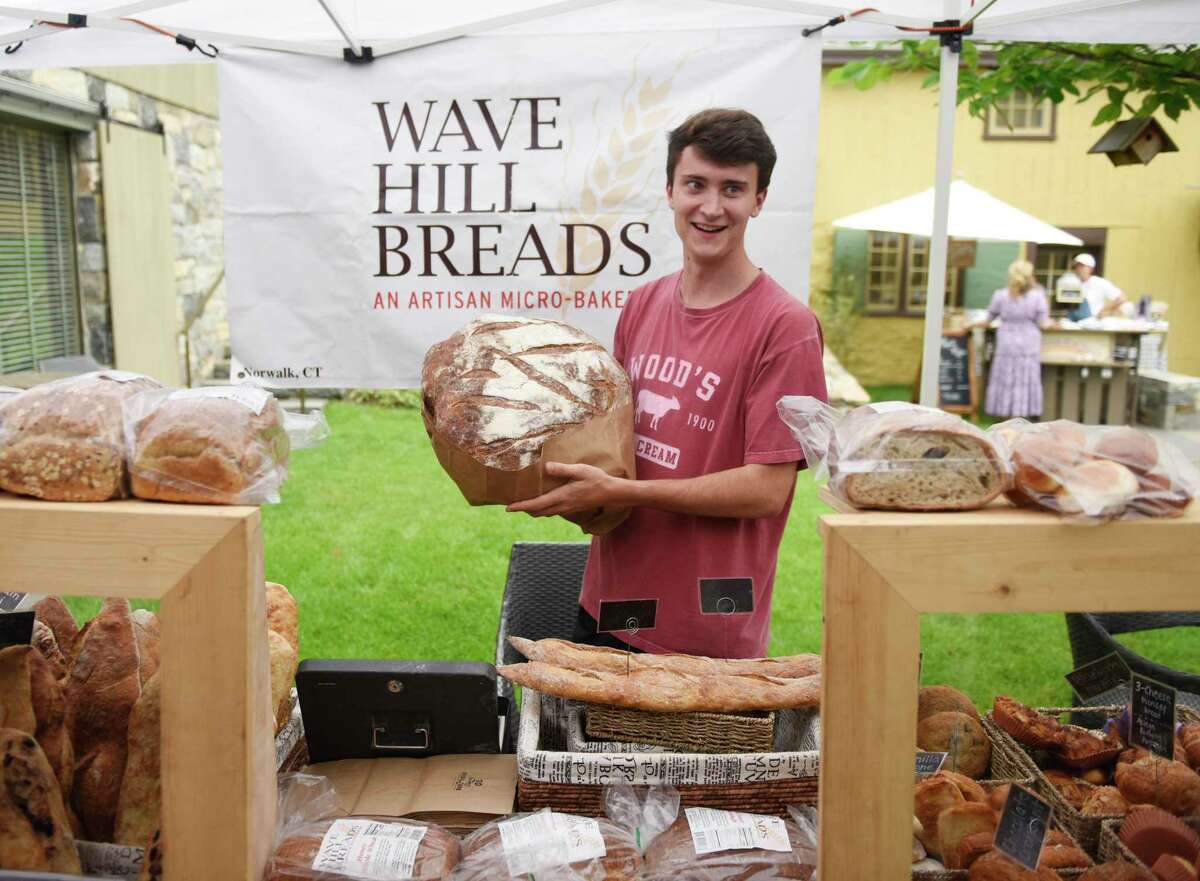Andrew Santacroce holds a huge sourdough loaf at the Norwalk-based Wave Hill Bread stand at the Tavern Garden Market at the Greenwich Historical Society in the Cos Cob section of Greenwich, Conn. Wednesday, July 14, 2021. On alternating Wednesdays from May through November, vendors sell a variety of market items such as produce, sweets, bread, gifts, crafts, and flowers. The market is held outdoors in the garden when weather permits, and indoors in the lobby when it rains.