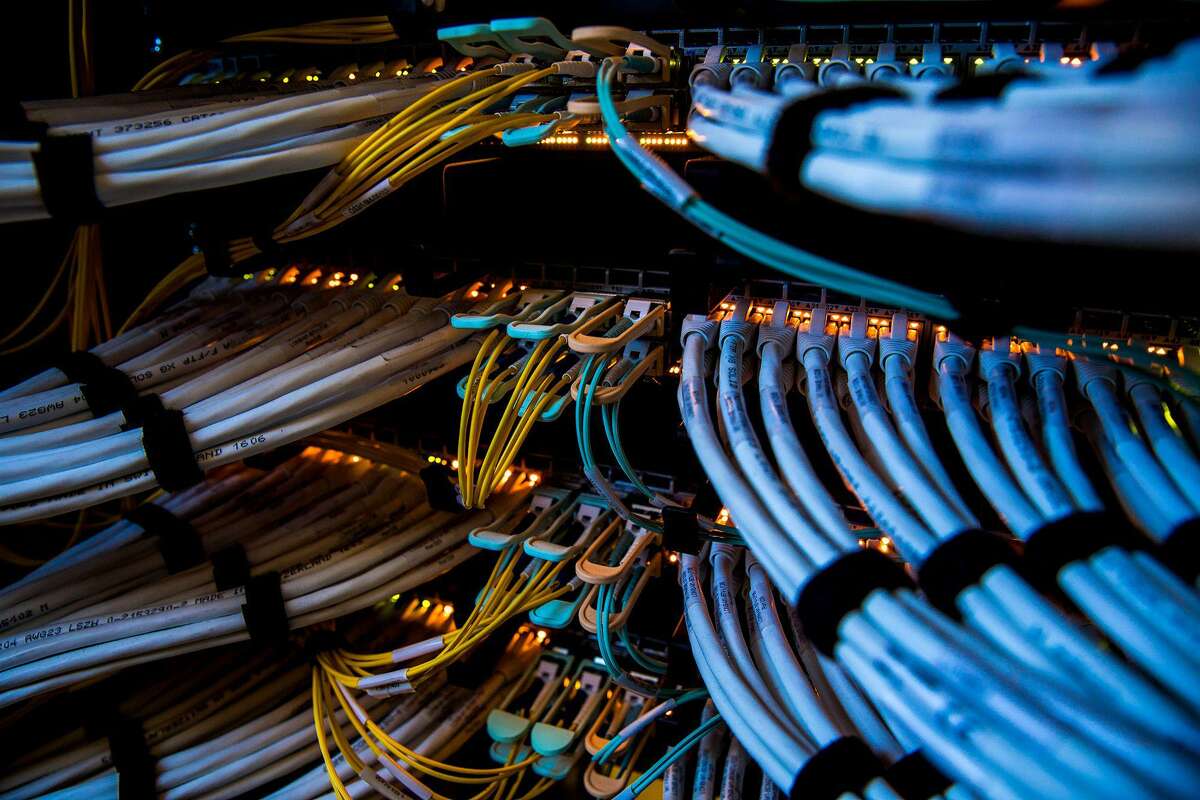 Fiber-optic cables, center, and copper Ethernet cables feed into switches inside a communications room at an office in London.