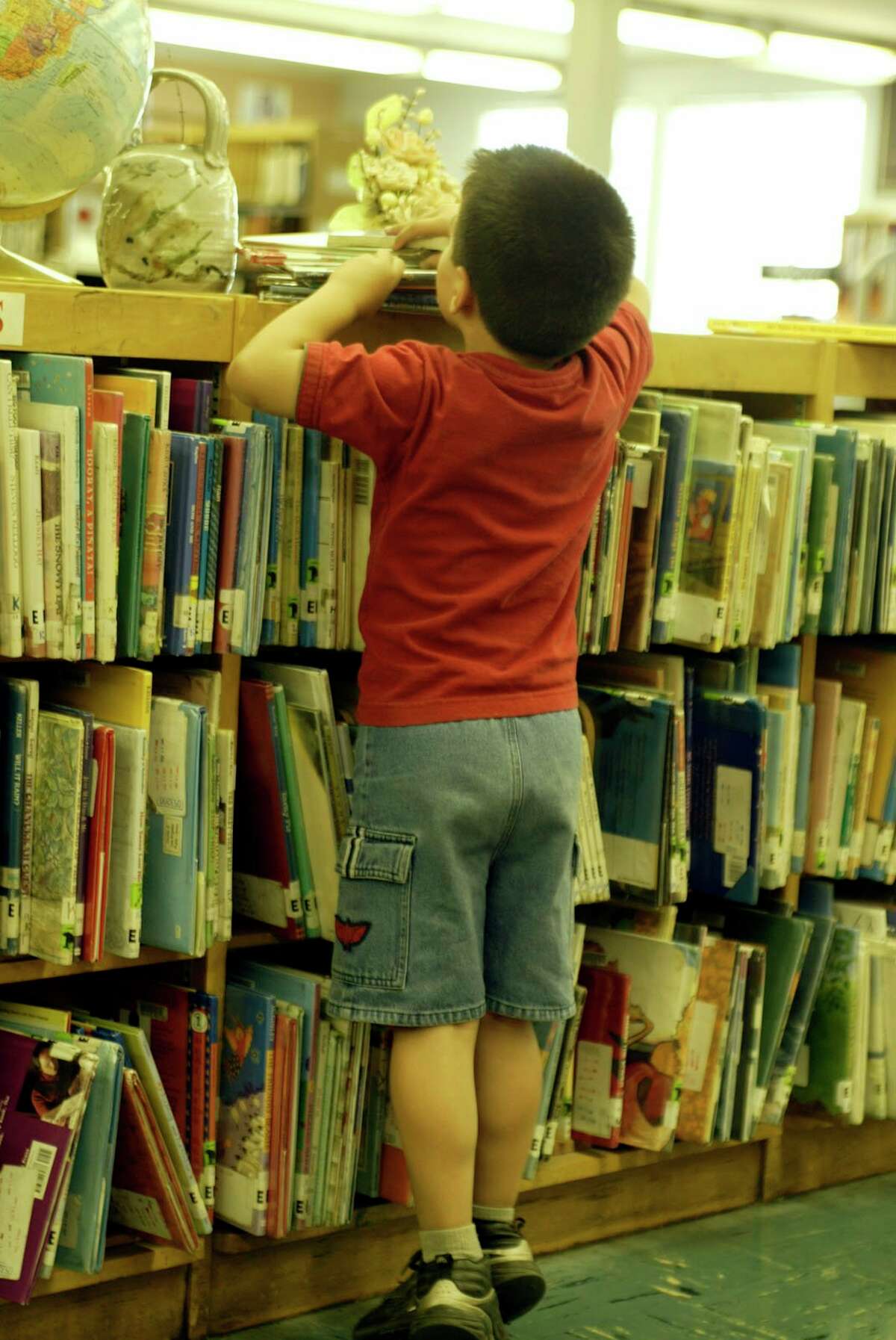 A 4-year-old kid looks at the stack of books he is collecting with his mother and sister. (Photo by Annie Wells/Los Angeles Times via Getty Images)
