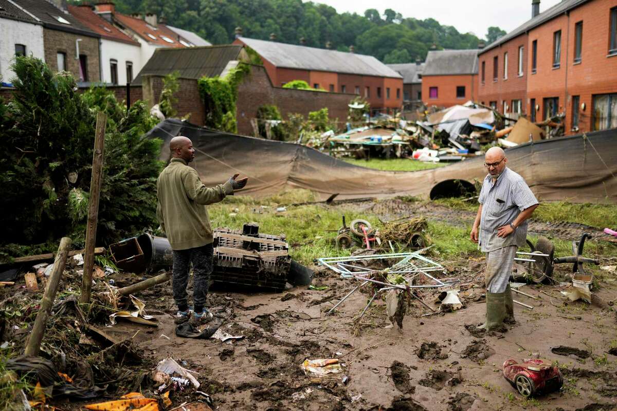 Two residents speak with each other as they clean up after flooding in Ensival, Verviers, Belgium, Friday July 16, 2021. Severe flooding in Germany and Belgium has turned streams and streets into raging torrents that have swept away cars and caused houses to collapse.