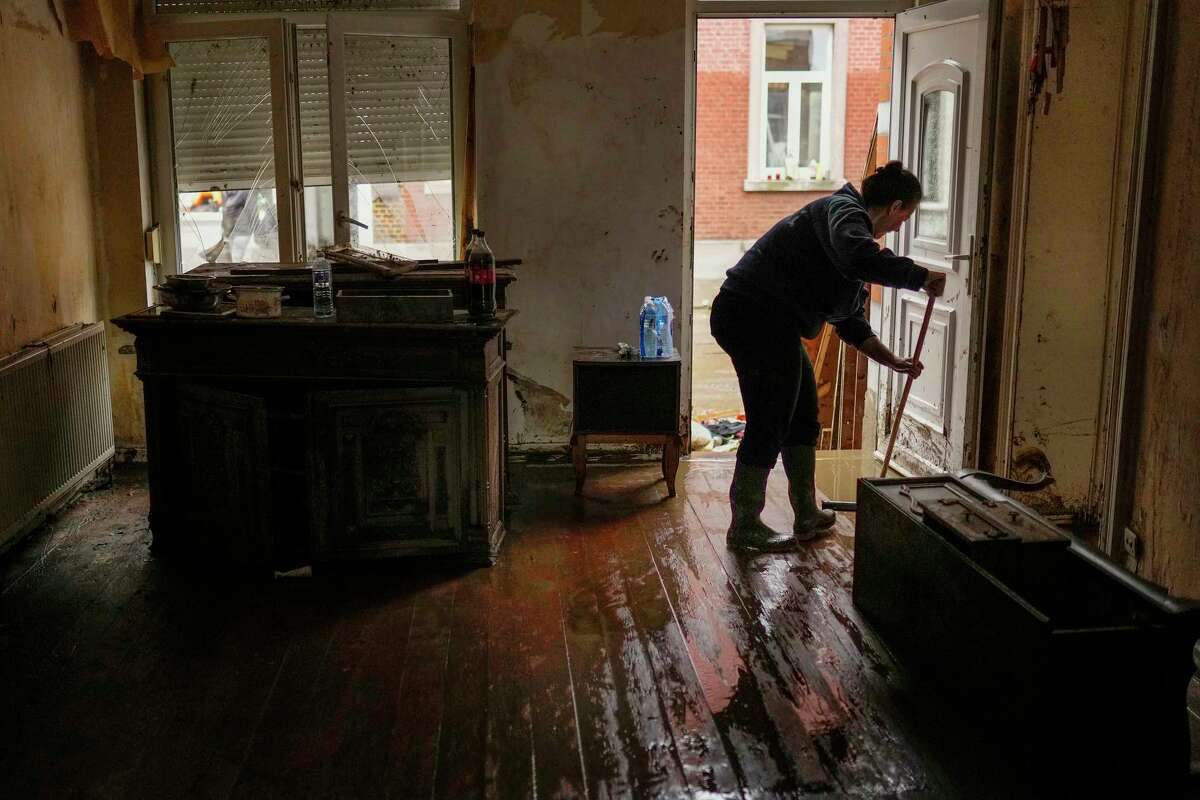 A resident sweeps mud and water out of her house after flooding in Ensival, Verviers, Belgium, Friday July 16, 2021. Severe flooding in Germany and Belgium has turned streams and streets into raging torrents that have swept away cars and caused houses to collapse.