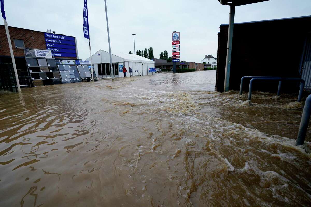 People wade through a flooded street in Tienen, Belgium, Friday, July 16, 2021. Severe flooding in Germany and Belgium has turned streams and streets into raging torrents that have swept away cars and caused houses to collapse.