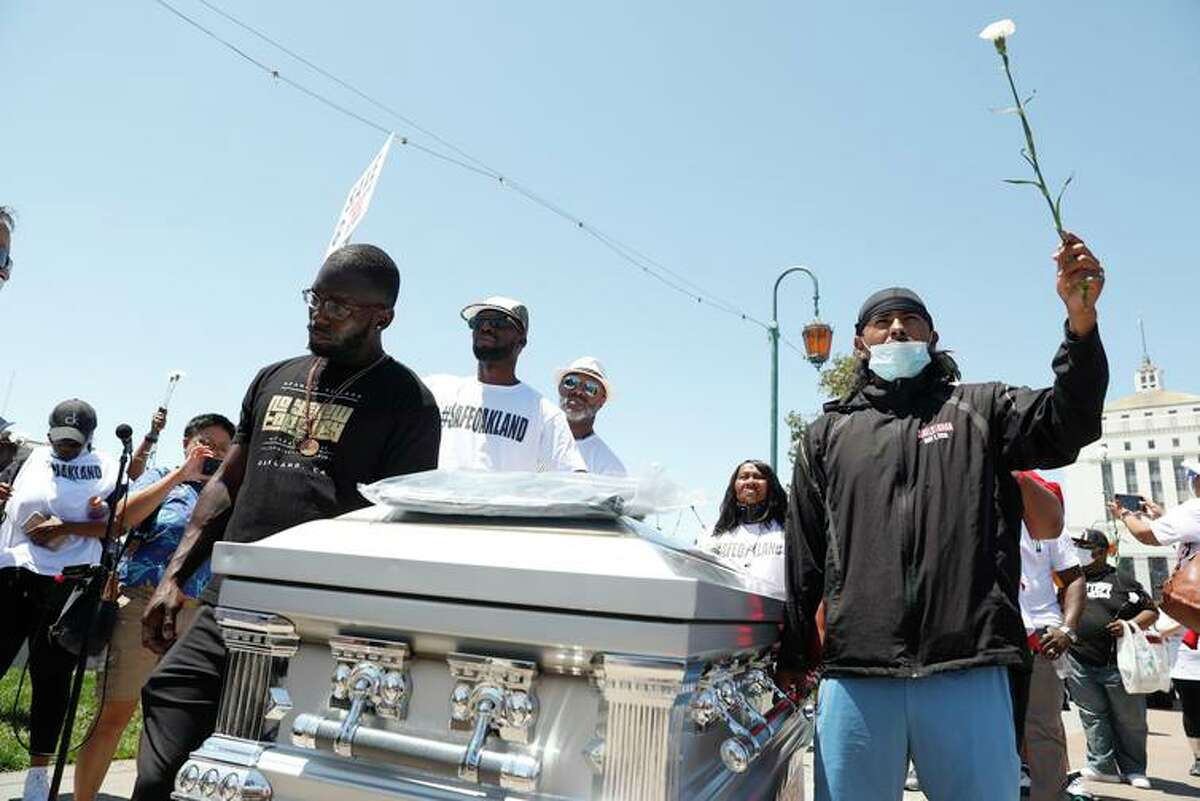 7月10日，在“为奥克兰安全挺身而出”的集会上，寻求暴力解决方案的非营利组织亚当米卡村的成员们正在移动象征着枪支受害者的棺材。