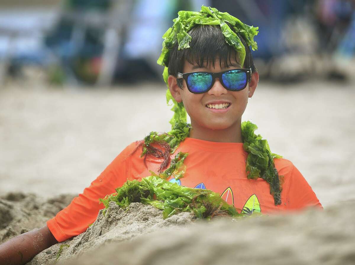 James Lee, 14, of Milford, goes the extra mile burying himself in the sand and covered in seaweed to portray a merman during the annual sand sculpture competition at Walnut Beach in Milford Conn. on Sunday, July 18, 2021. Live judging was cancelled for fear of rain, but contestants were still able to submit photographs of their finished sculptures for judging in a virtual competition.
