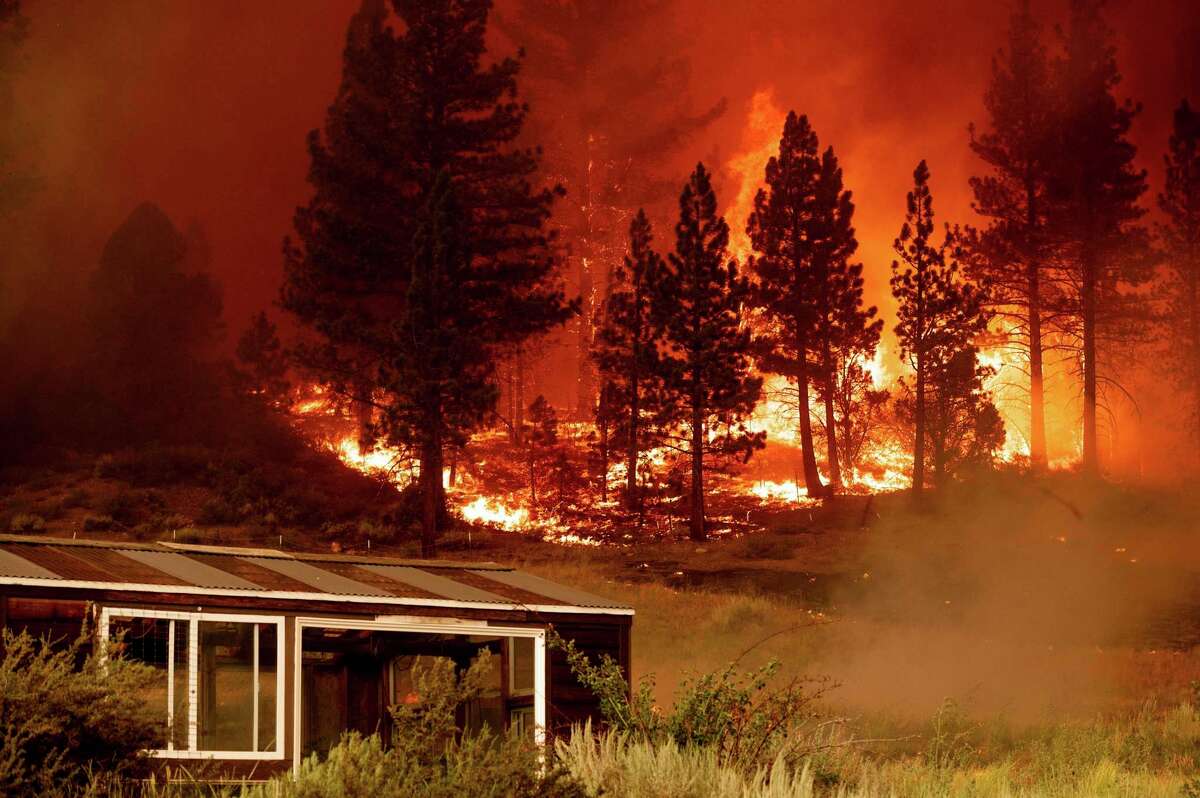 The Tamarack Fire burns behind a greenhouse in Markleeville in July 2021. The U.S. Forest Service was accused of letting the fire burn on its own for too long, but defended its response, saying it was putting out fires elsewhere. Critics jumped on the blaze as an example of irresponsible “let-it-burn” policy.
