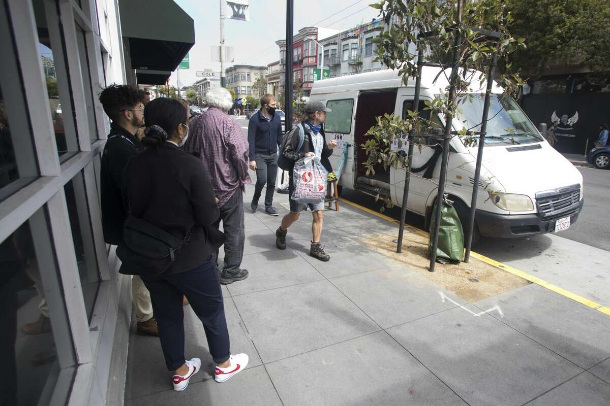 A crowd of pedestrians hears Brandy Collins, whose performance name is Mr. Brandy, playing the piano in the back seat of his Sprinter van on July 16, 2021 in Haight-Ashbury, San Francisco.