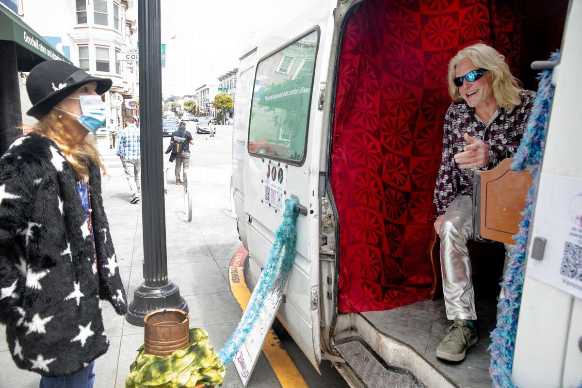 Brandy Collins, whose name is Mr. Brandy, greets a fan after playing a song on a piano in the back of his Sprinter van in the Haight-Ashbury neighborhood of San Francisco on July 16, 2021.