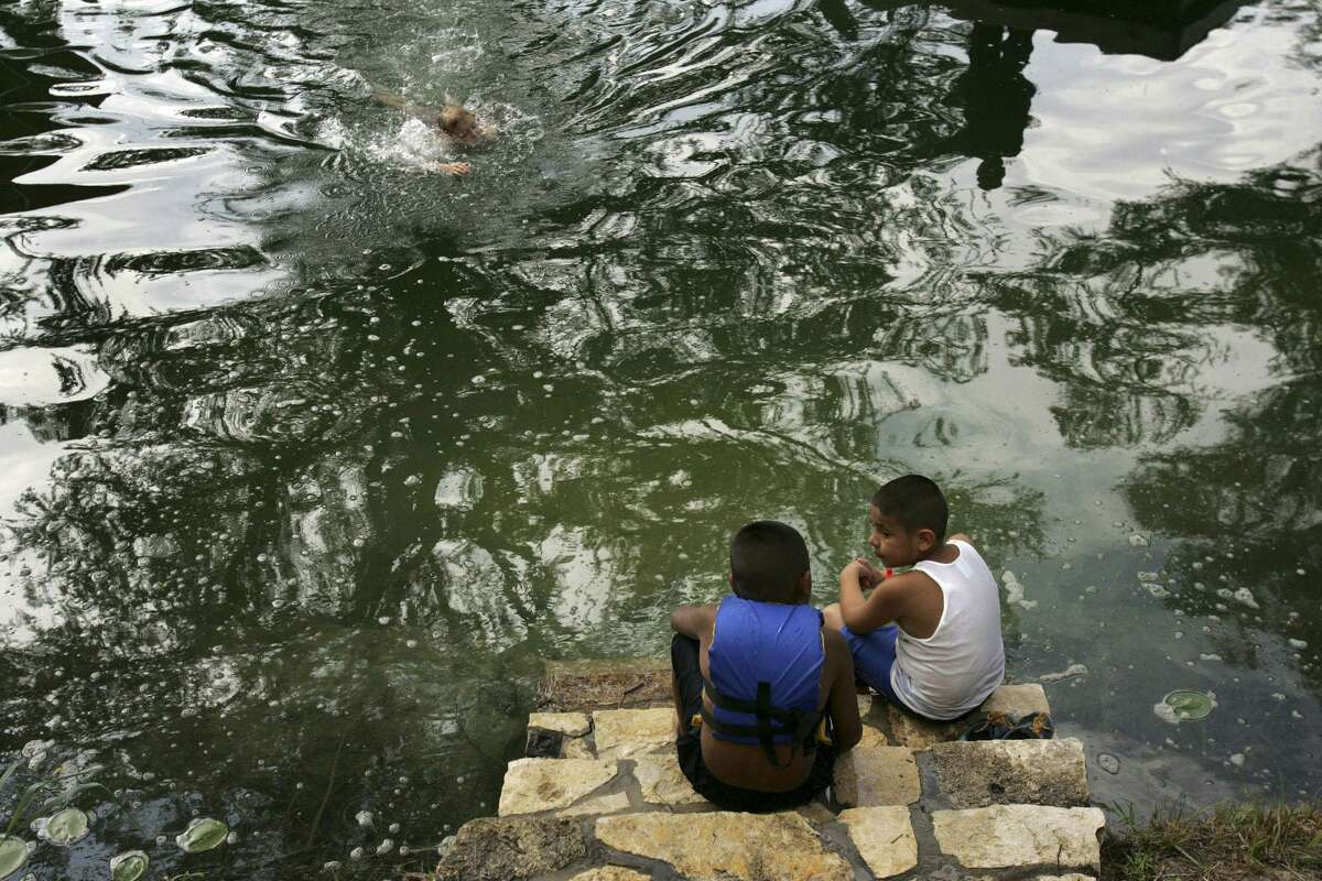 In this 2005 photo, San Antonio Housing Authority residents Michael Jimenez, 7, left, and Eddie Gonzales, 8, watch fellow campers slide into the Guadalupe River at YMCA Camp Flaming Arrow in Hunt. Open since 1927, the camp is closing this year.