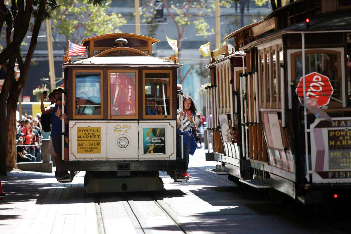 Passengers hold on to the side of a cable car as it passes other cable cars as it moves up Powell Street from the cable car turnaround at Market Street in San Francisco. During the month of August, all cable cars will be free for riders.