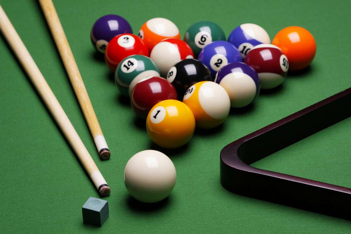 The photo shows the composition of billiard balls on a table with a triangle, balls and sticks and elements to the game of billiards. 