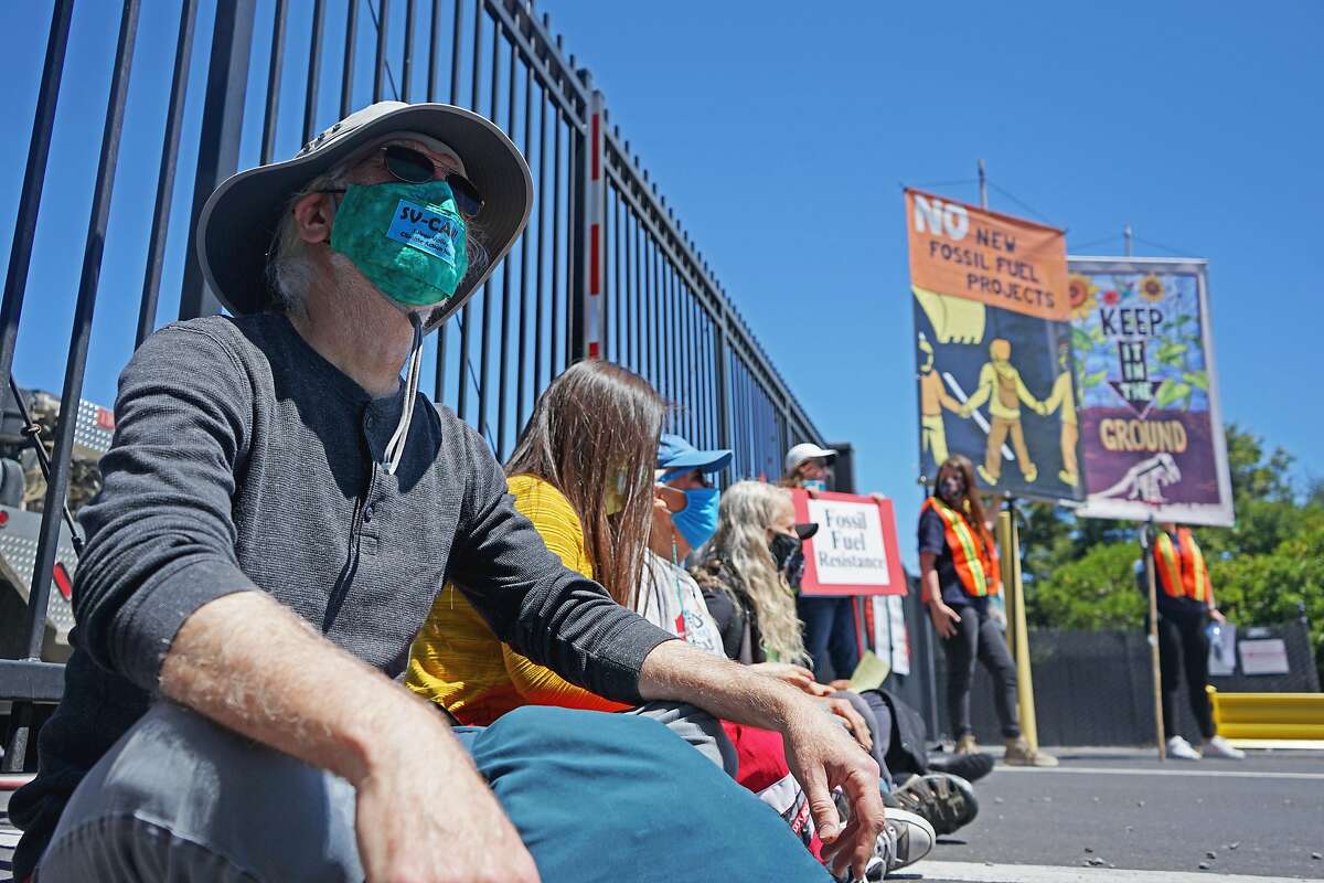 A group of activists sit in front of the Castro Street gate entrance of the Chevron oil refinery in Richmond to block Chevron Fire Station vehicles from wetting the pavement where protesters started painting an art piece during the 8th annual Anti-Chevron Day at the Chevron refinery in Richmond, California on May 21, 2021.