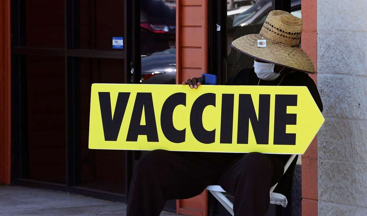A seated man wearing a face mask holds a sign pointing to a mobile vaccination clinic on July 16, 2021, along Crenshaw Boulevard in Los Angeles, California.