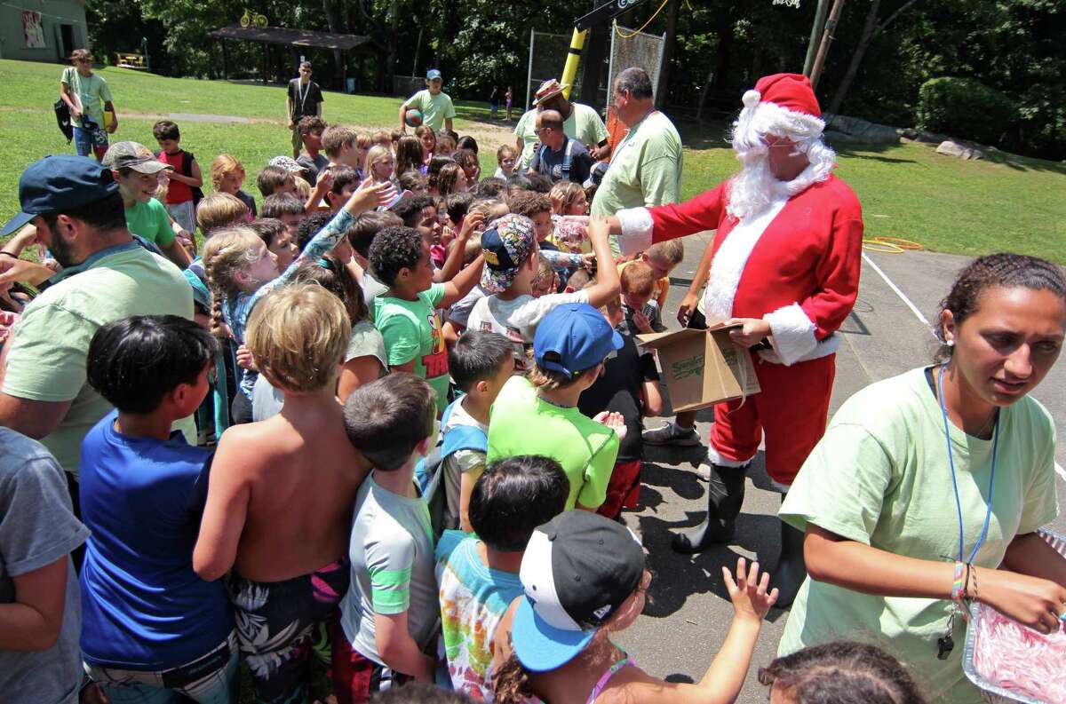 Santa hands out candy canes after arriving on a firetruck during the Boys and Girls Club of Greenwich summer camp's annual Christmas in July tradition at Camp Simmons in Greenwich, Conn., on Friday July 23, 2021.After handing out the candy, a firehose was used to cool the kids off.