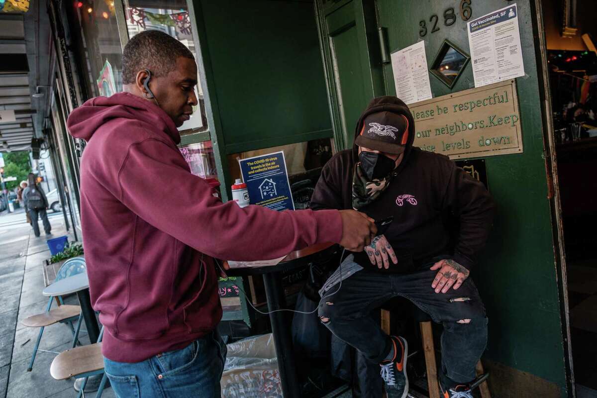 Manny B. shows proof of vaccination to doorman Jason Voisine at the Latin America Club in San Francisco. Berkeley is joining San Francisco in requiring proof of vaccination for many indoor activities, such as dining.
