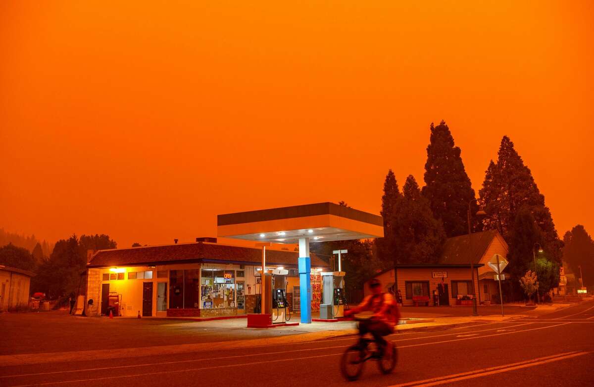 A man rides his bike passed a gas station as smoke fills the sky during the Dixie fire in Greenville, California on July 23, 2021. 