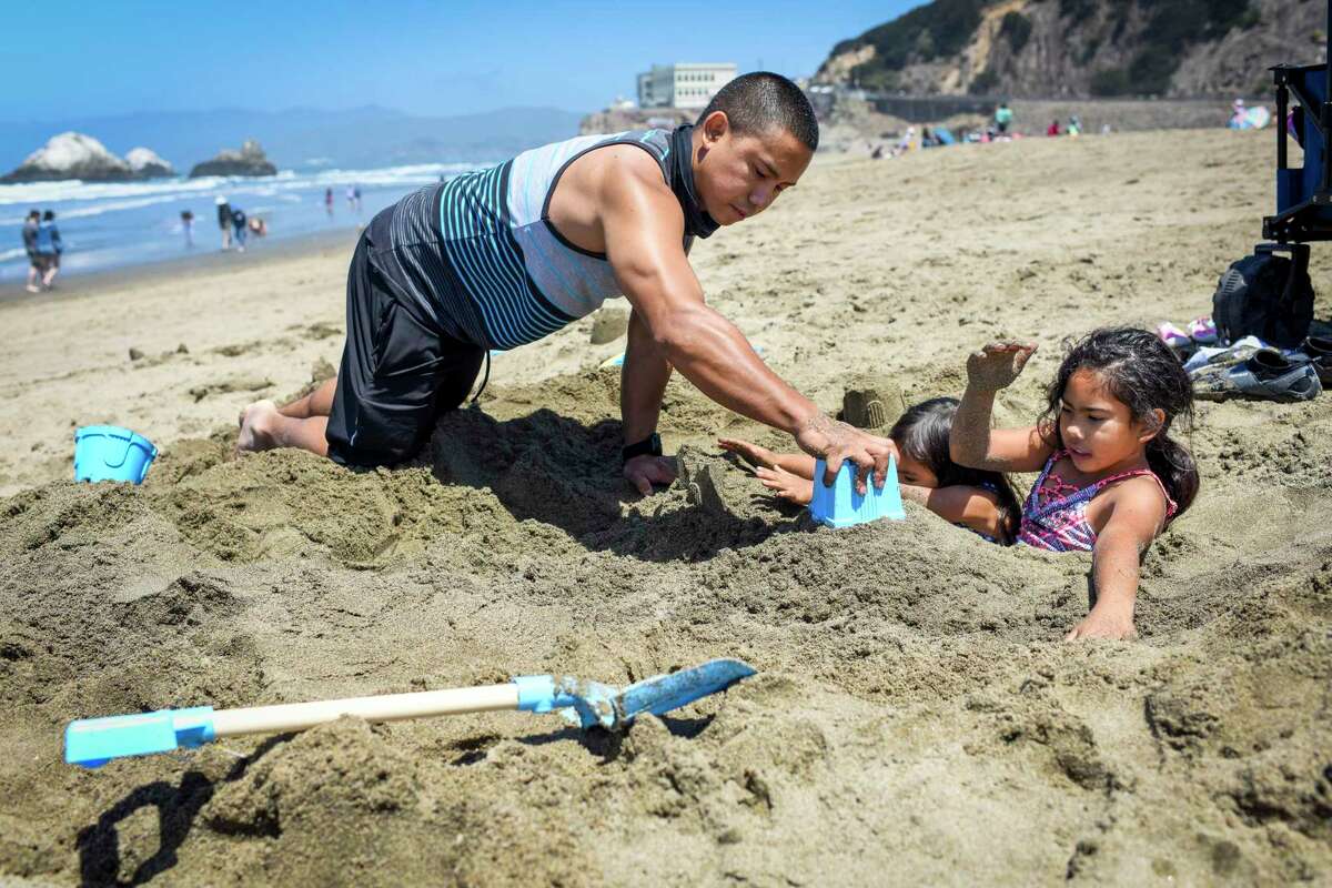 Tyrone Keller of Sacramento and his daughters, Nayeli Keller (right), age 9, and Mia Keller (second from right), age 4, play in the sand at Ocean Beach in San Francisco, Calif. on Monday, May 31, 2021.