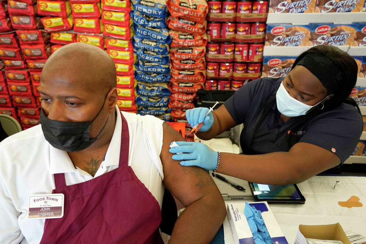 John Jones, cashier, left, receiveS a Pfizer vaccination from Kiosha Martin, LVN, right, with Houston Health Department, during an event held at Food Town, 5367 Antoine Dr., Tuesday, July 27, 2021 in Houston.