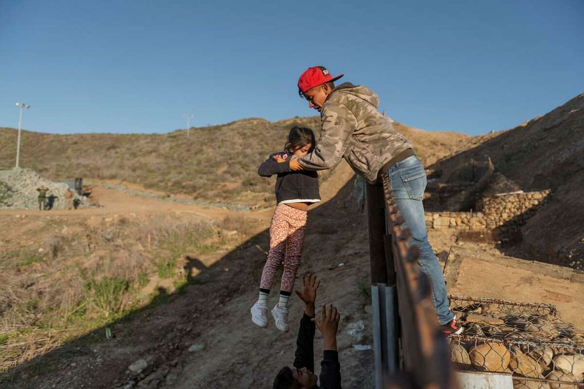 A migrant from Honduras passes a child to her father after he jumped the border fence from Tijuana to get into the U.S.