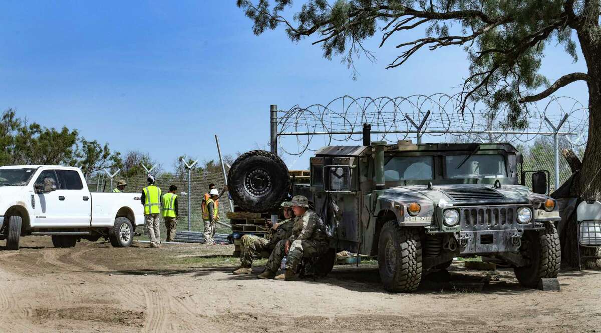 Members of the Texas National Guard take shelter from the heat by their vehicle as a crew installs new fencing on the border near Del Rio on Wednesday. Gov. Greg Abbott has escalated the role of the guard and Department of Public Safety in an effort to stop the migration.