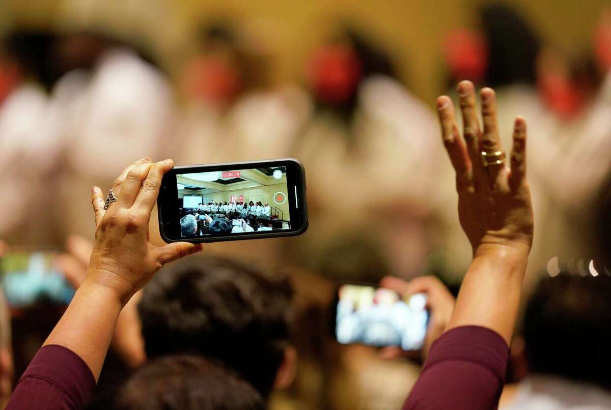 A woman video records and waves as the University of Houston medical students recite their student oath during the White Coat Ceremony held at the Hilton UH Saturday, July 31, 2021 in Houston.