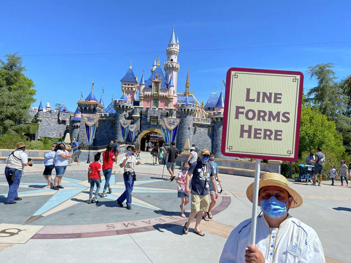 A Disneyland employee forms a line for visitors to take pictures in front of Sleeping Beauty Castle in Anaheim, Calif., on Friday, April 30, 2021.