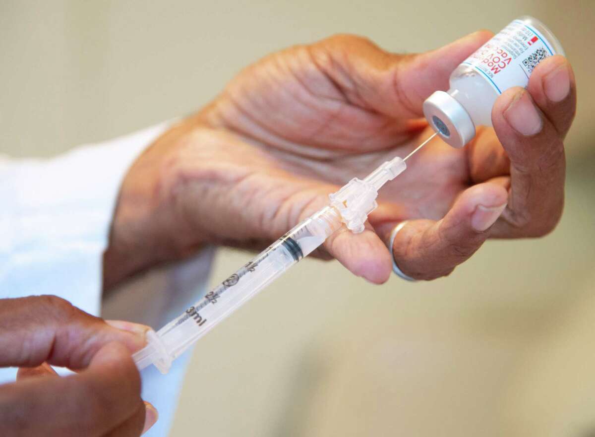 New COVID booster: Should you get the shot if you had symptoms? Family physician Dr. Curtis Robinson prepares a dose of the Moderna COVID-19 vaccine.