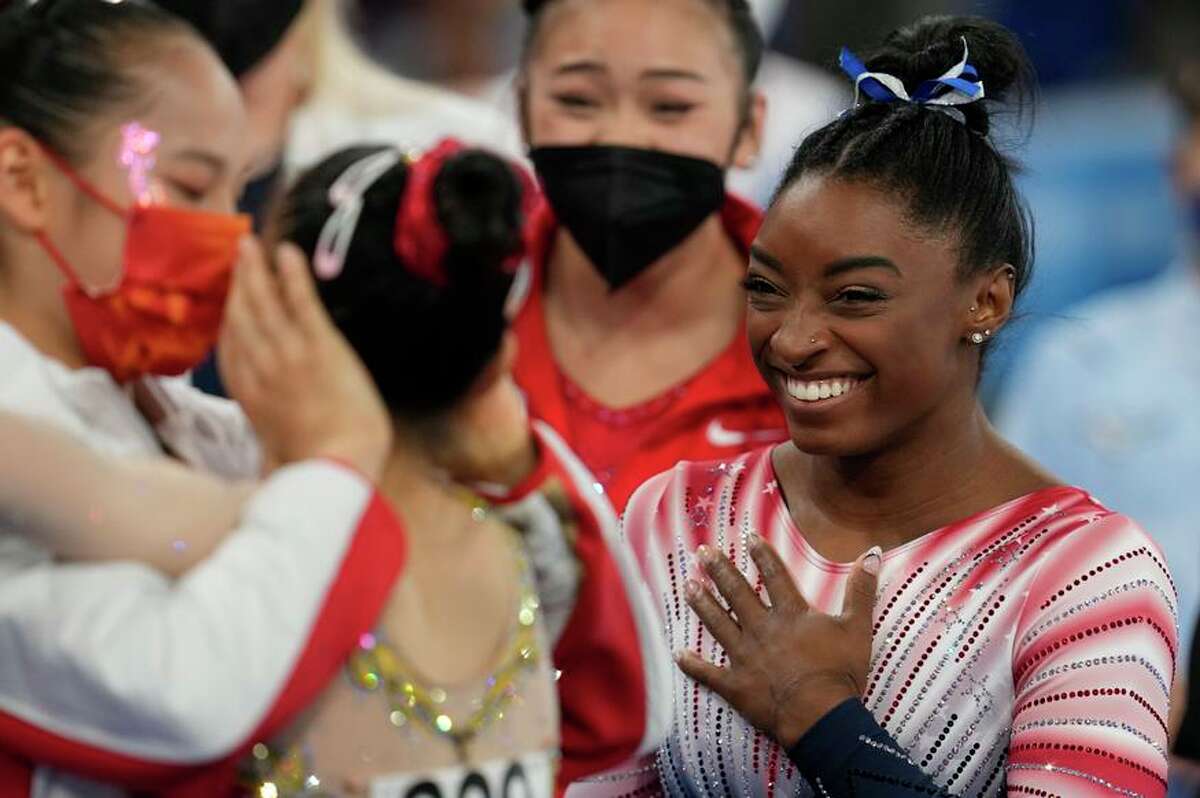 Simone Biles, of the United States, smiles as Tang Xijing, of China, left, embraces teammate Guan Chenchen after the latter won the gold medal on the balance beam during the artistic gymnastics women's apparatus final at the 2020 Summer Olympics, Tuesday, Aug. 3, 2021, in Tokyo, Japan. Biles won the bronze medal. (AP Photo/Natacha Pisarenko)
