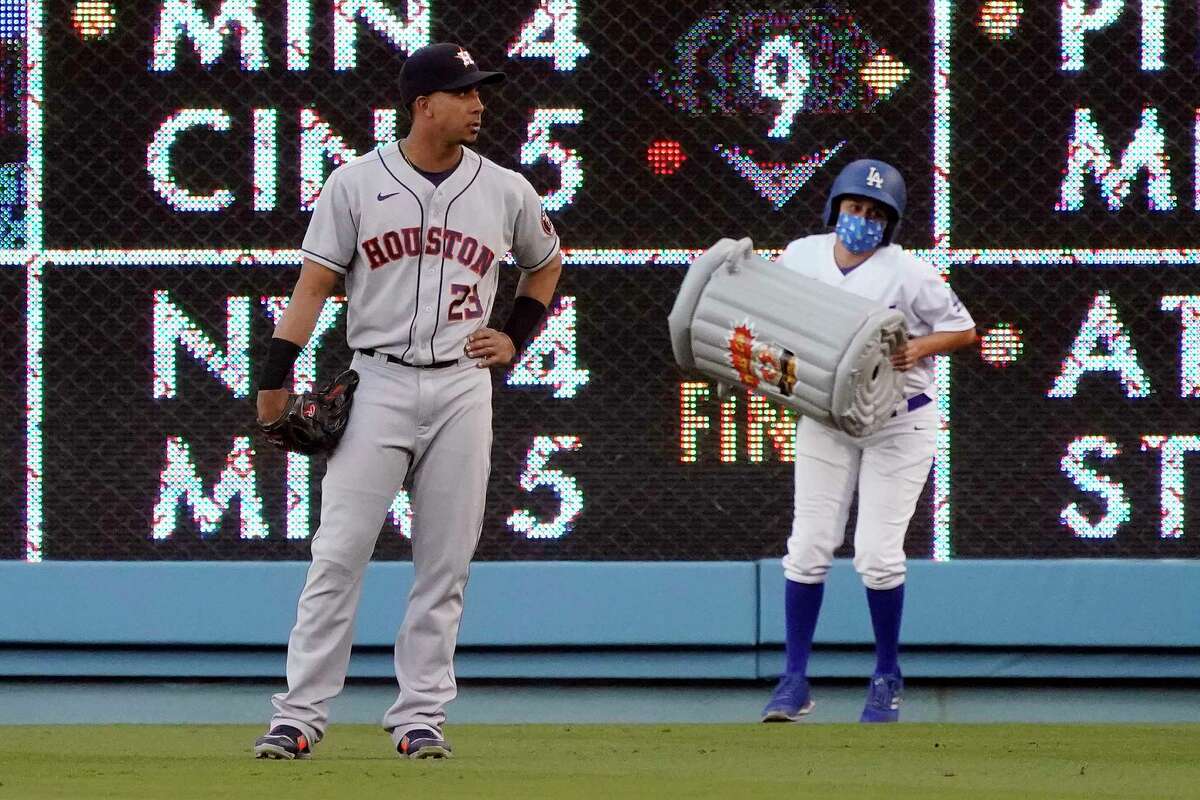 A ball girl removes an inflatable item in the shape of a trash can behind Houston Astros right fielder Michael Brantley during the first inning of the Astros' baseball game against the Los Angeles Dodgers on Tuesday, Aug. 3, 2021, in Los Angeles. (AP Photo/Marcio Jose Sanchez)