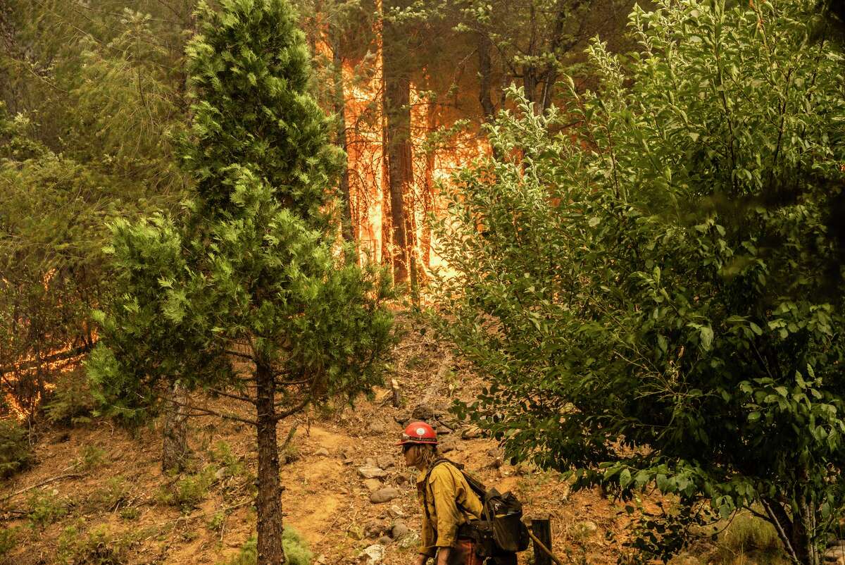 A firefighter with the Stanislaus Hotshots walks past a backfire while defending a home from the Dixie Fire in Greenville in the Sierra north of Lake Tahoe.