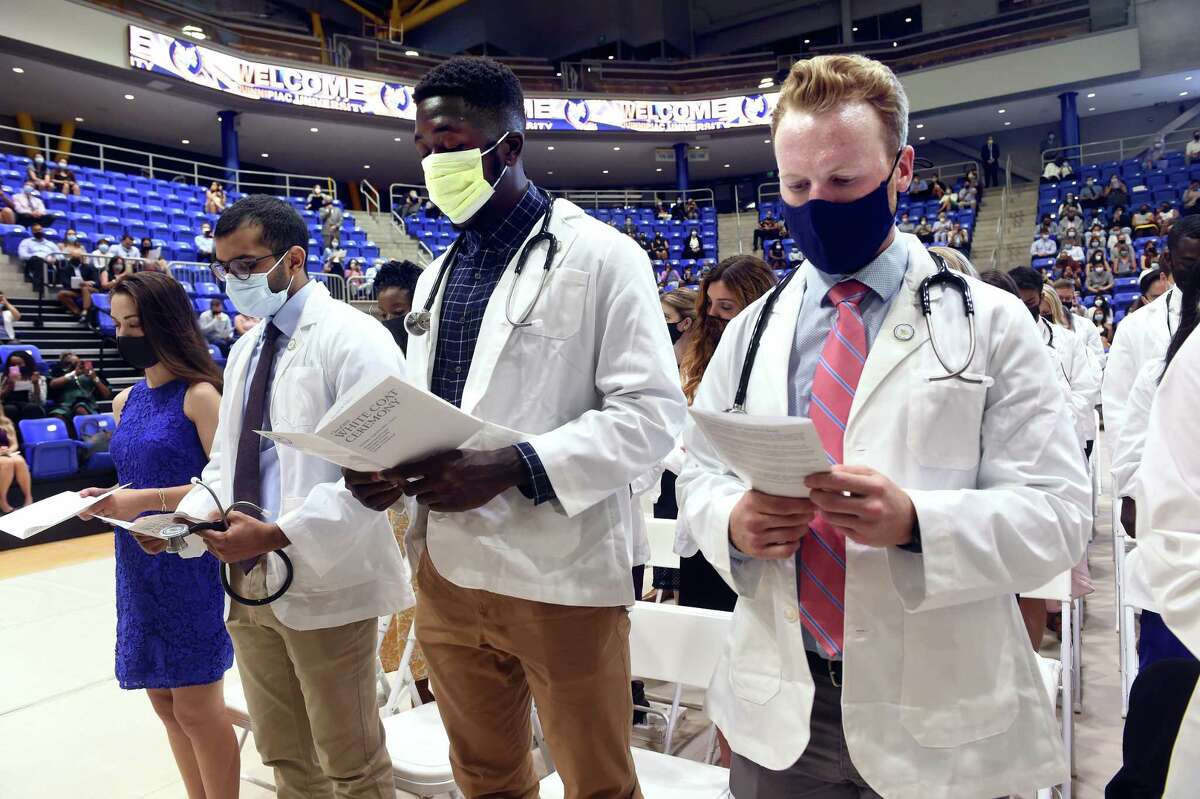 From left in white coats, Hatim Amiji, Adebowale Babalola and John Baekey recite the Hippocratic Oath during the class of 2025 White Coat Ceremony at Quinnipiac University's People's United Center in Hamden Aug. 5, 2021.