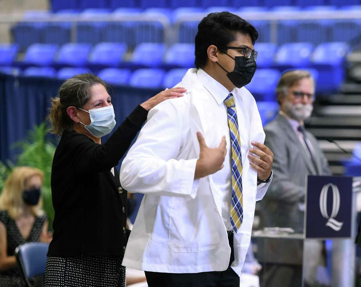 Dr. Lisa Conti, left, assists Arun Narikatte with his white coat during the class of 2025 White Coat Ceremony at Quinnipiac University's People's United Center in Hamden Aug. 5, 2021.
