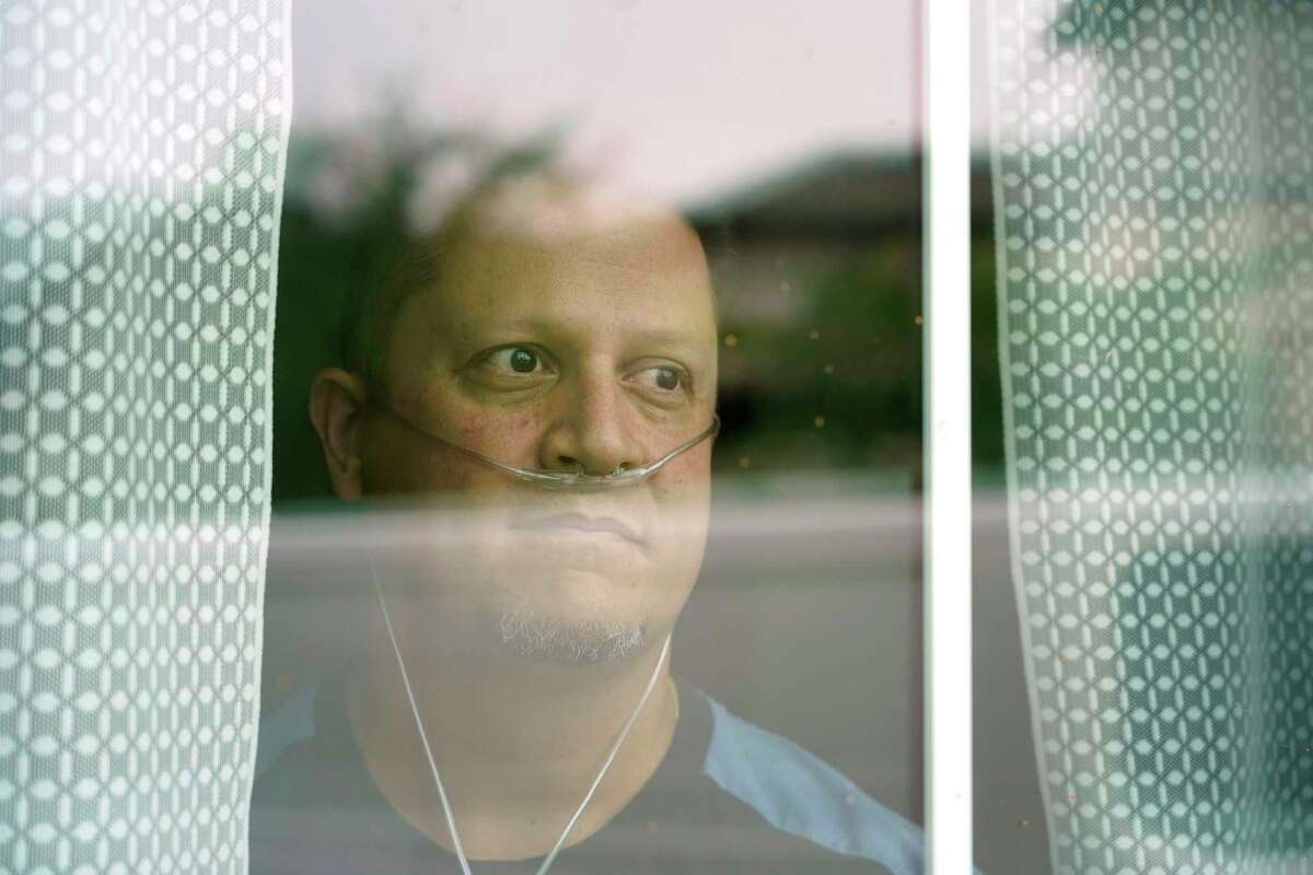 Andres Perekalski looks through the window of his home Thursday, Aug. 5, 2021 in Cypress, where he is quarantined from COVID-19. He spent two weeks in a COVID ICU. He regrets not being vaccinated and wants others to learn from his mistake.