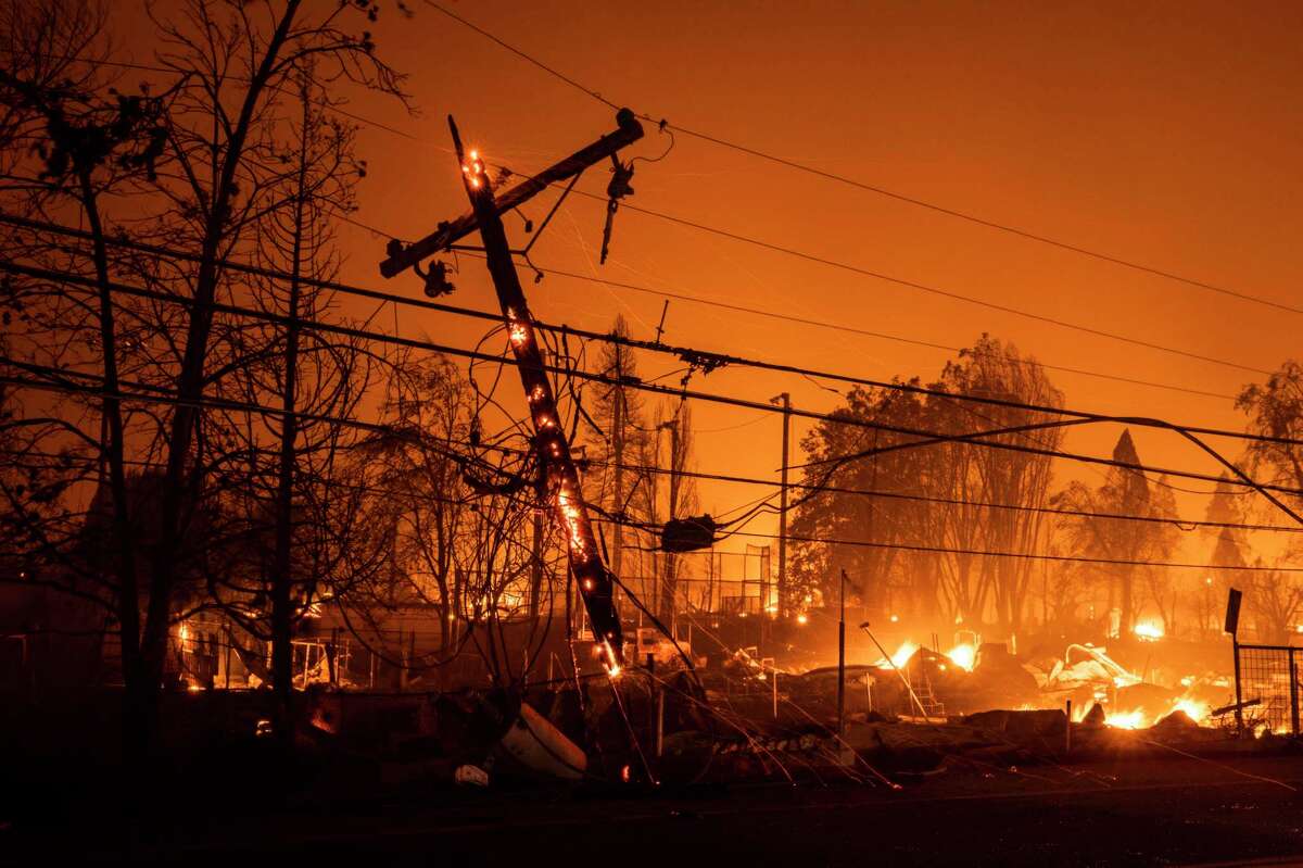 A utility pole smolders Aug. 4 as properties burn nearby during the Dixie Fire in Greenville (Plumas County). PG&E was blamed for starting the massive fire.