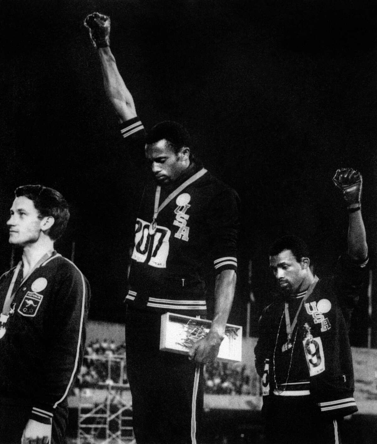 US athletes Tommie Smith (C) and John Carlos (R) raise their gloved fists in the Black Power salute to express their opposition to racism in the USA during the US national anthem, after receiving their medals 17 October 1968 for first and third place in the men's 200m event at the Mexico Olympic Games. At left is Peter Norman of Australia who took second place. The HBO Sports documentary Fists of Freedom: The Story of the '68 Summer Games explores one of the most powerful moments in sport this century