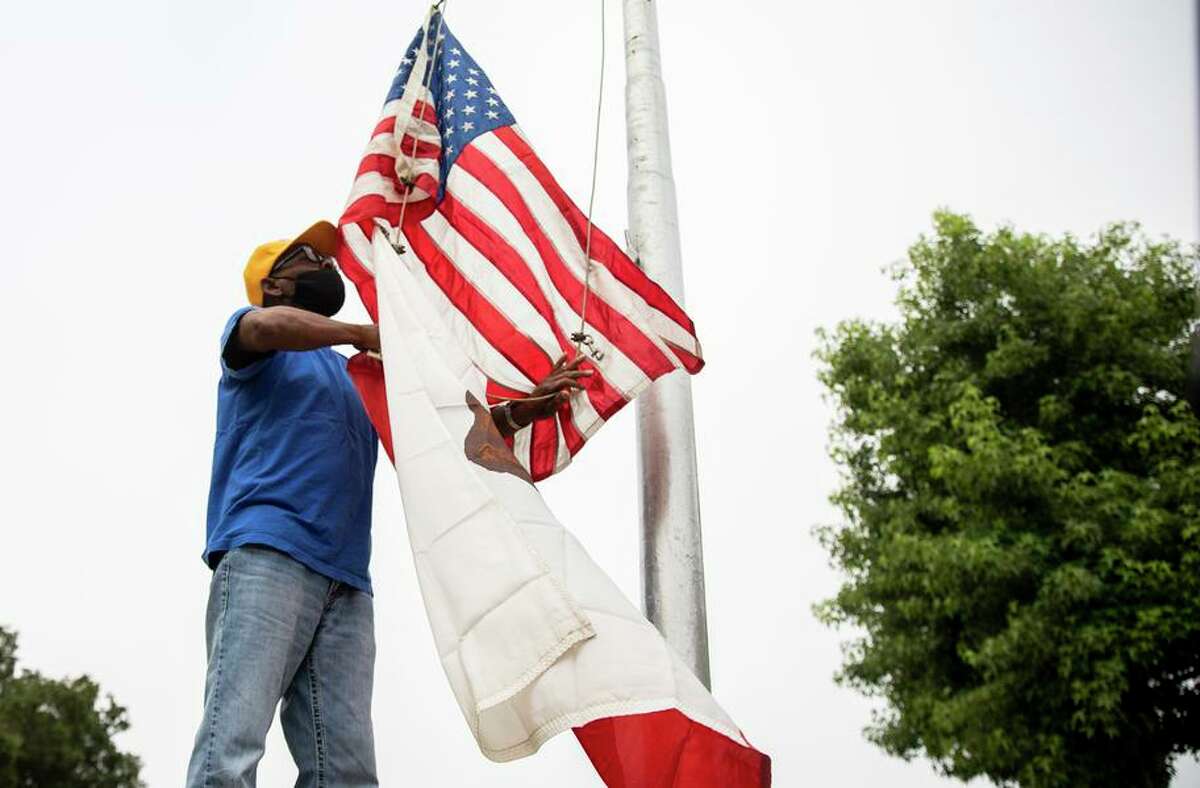 Oakland resident and veteran Ken McNeal raises flags as students arrive for the first day at Howard Elementary School.