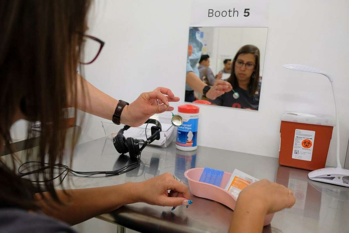 In this photo taken Wednesday, Aug. 29, 2018, volunteer Rachele Huennekens sits at a booth injection station during a demonstration at Safer Inside, a realistic model of a safe injection site in San Francisco. The model is an example of a supervised, indoor location where intravenous drug users can consume drugs in safer conditions and access treatment and recovery services.