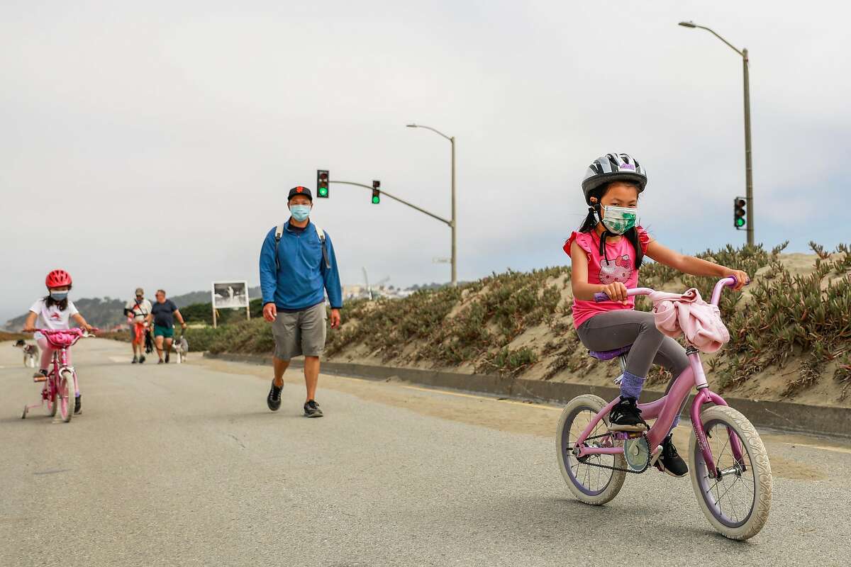 Hazel Ho, 4 father Tung Ho (center) and sister Zoe Ho, 6 (right) ride their bikes and walk on Great Highway on Tuesday, Aug. 10, 2021 in San Francisco, California. This is the last full week of car-free Great Highway. On August 16, it returns to cars five days a week.