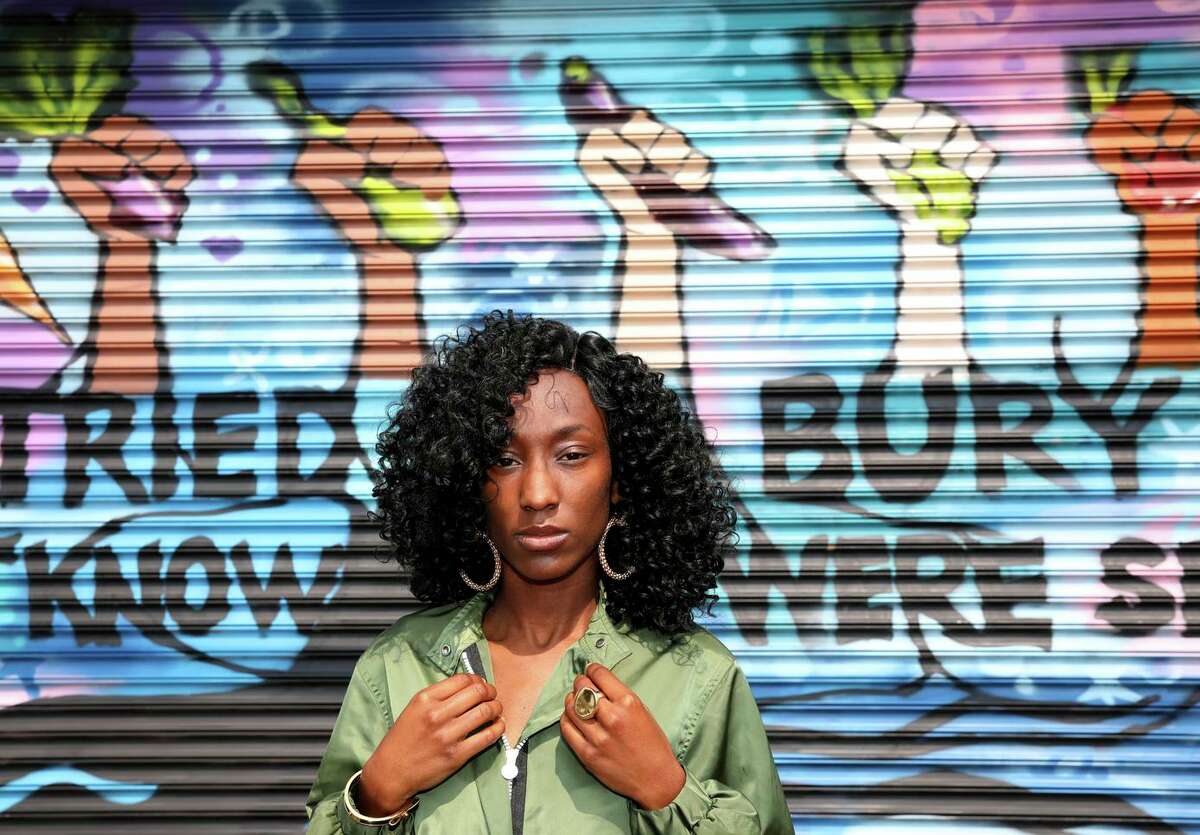 Keisha Henderson stands in front of a mural located outside the Handy Market in East Oakland on Friday, Aug. 6, 2021, in Oakland, Calif. The 29-year-old violence prevention activist has been helping to paint the mural on the corner store at the end of her block with a group called the Bay Area Mural Program.