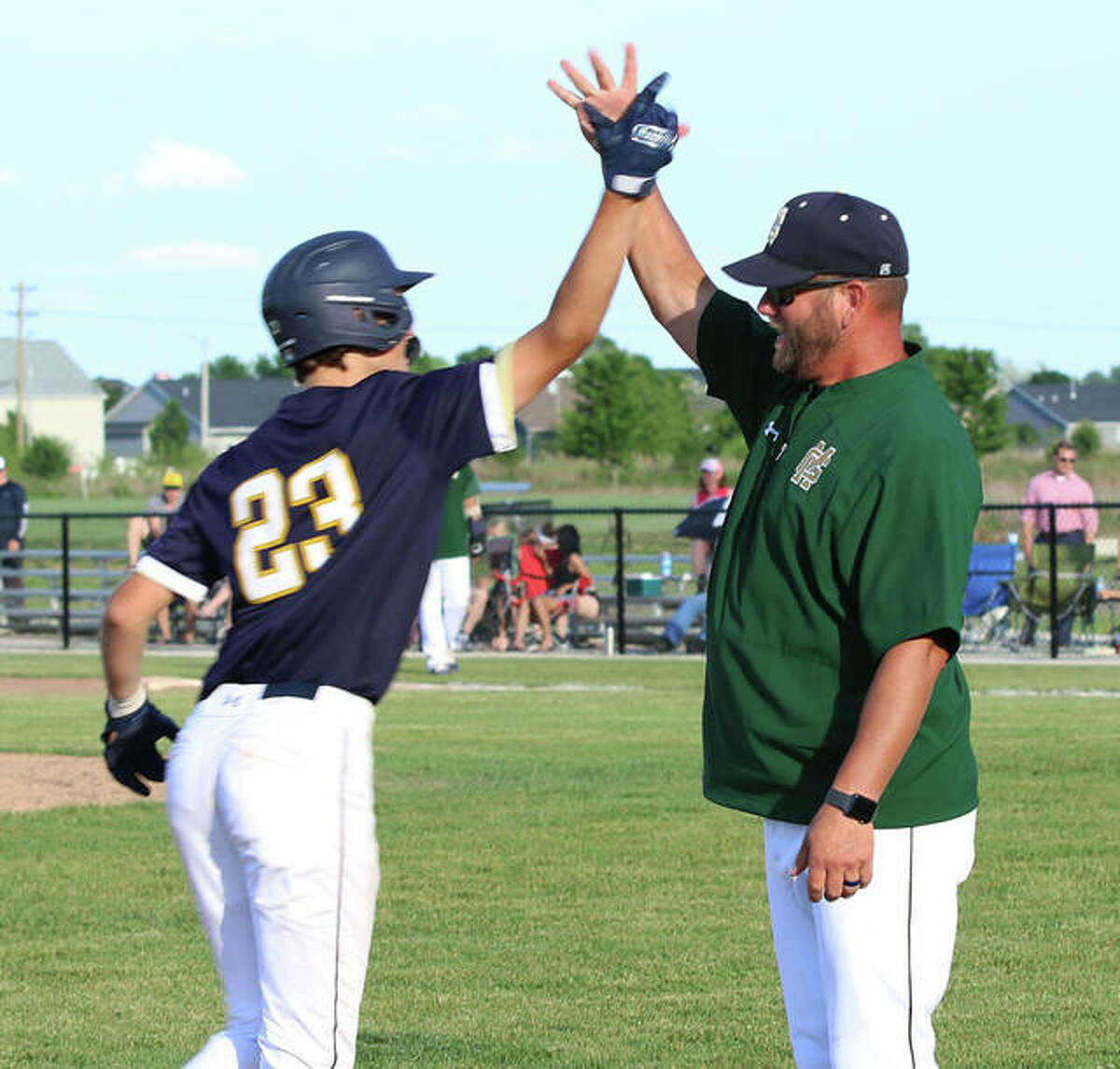 Father McGivney coach Chris Erwin (right) greets Jacob McKee rounding third base after McKee’s home run in a regional championship victory over Metro-East Lutheran on June 7 in Glen Carbon.