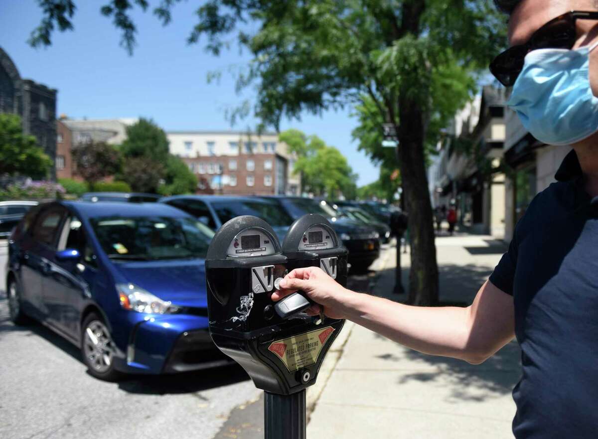 Stamford's Felice Donatiello puts a coin in a parking meter along Greenwich Avenue in downtown Greenwich, Conn. Monday, July 6, 2020. The town is looking to promote its permit program for downtown residents and businesses to keep those short-term spots open for customers like Donatiello.