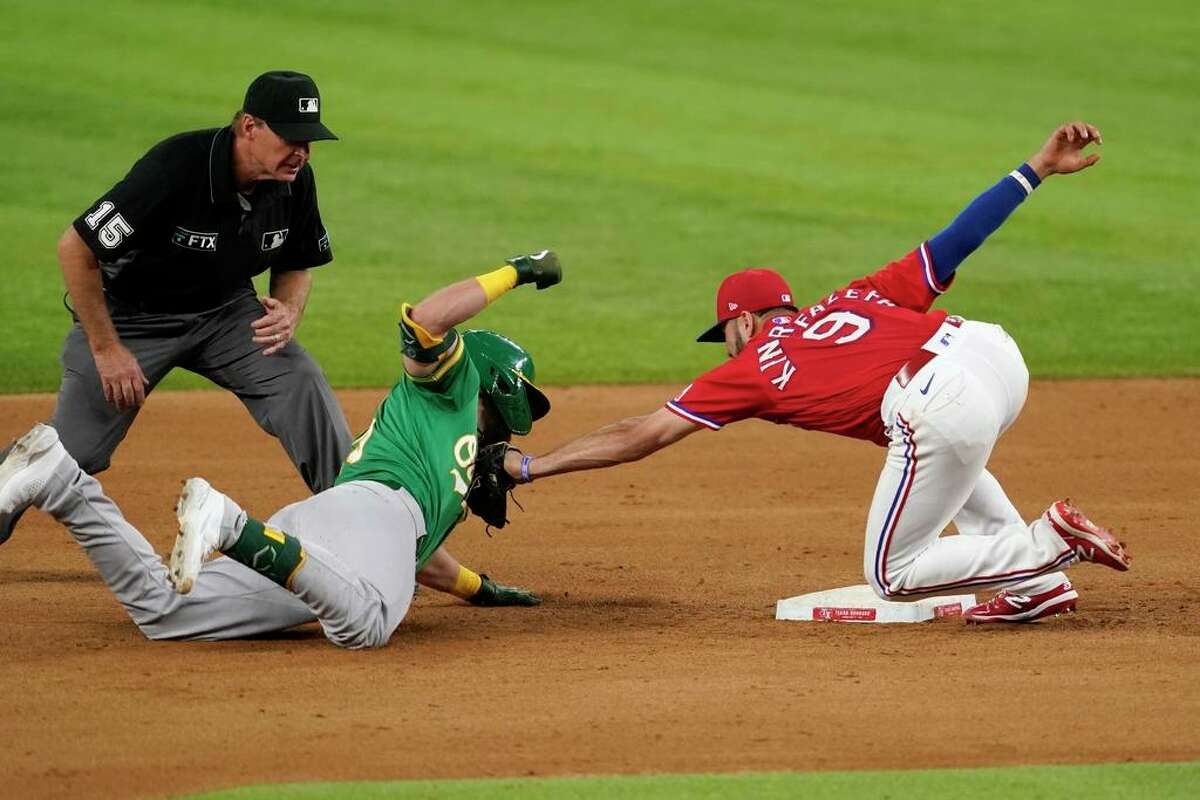 Oakland Athletics' Seth Brown, center, is tagged out by Texas Rangers third baseman Isiah Kiner-Falefa (9) as umpire Ed Hickox (15) watches in the eighth inning of a baseball game in Arlington, Texas, Friday, Aug. 13, 2021. Brown was tagged out while attempting to stretch out a run-scoring double that scored Matt Chapman. (AP Photo/Tony Gutierrez)