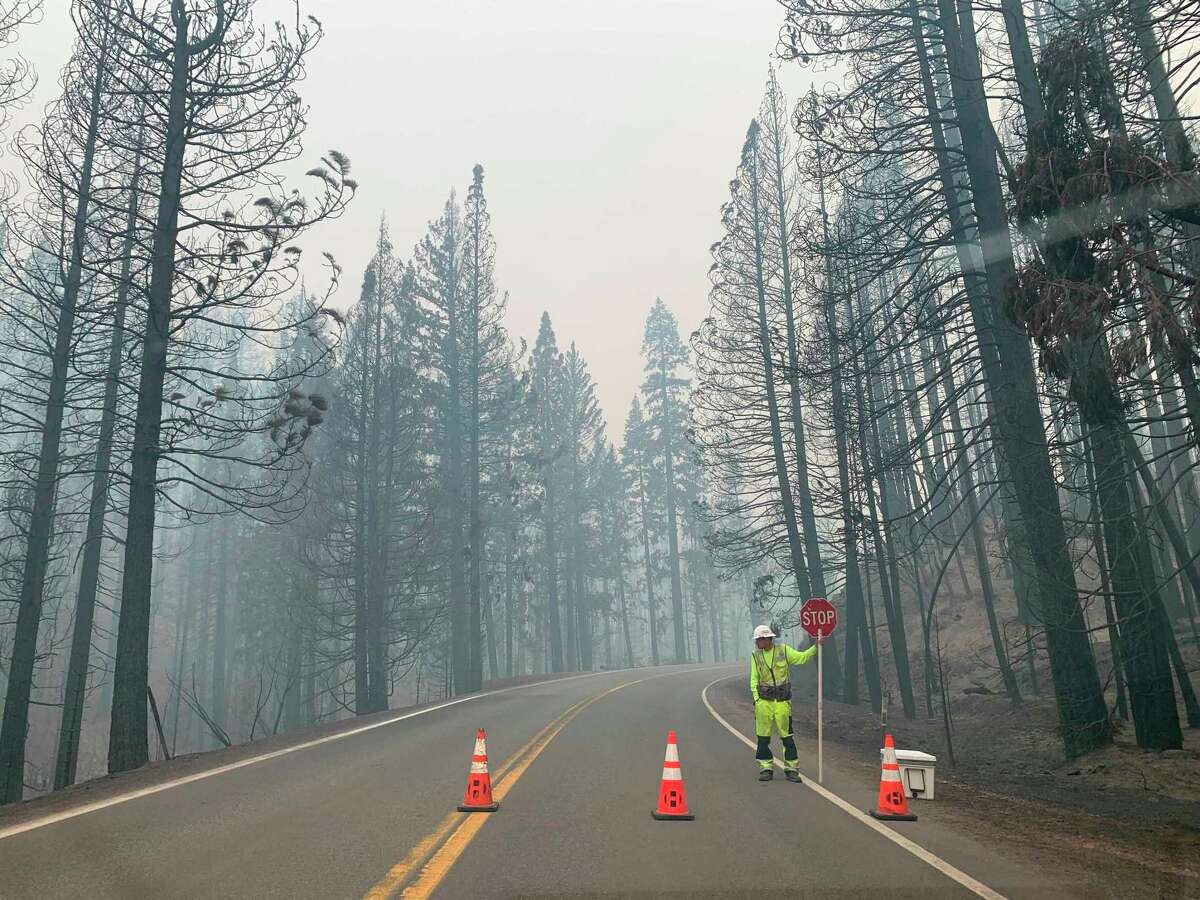 A worker blocks Highway 89 to Canyondam in Plumas County due to risk from the Dixie Fire, which also continues to rage across three other Northern California counties.