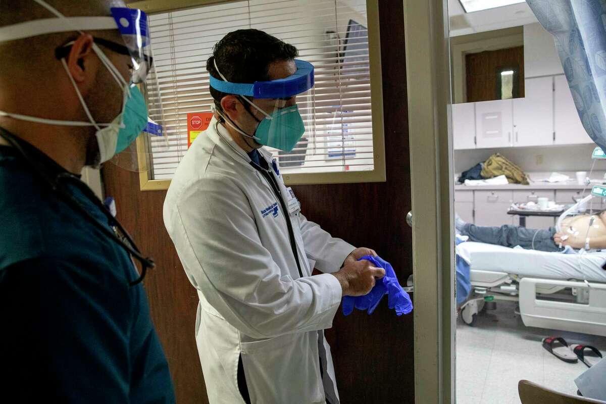 Dr. Oscar Rivera puts on gloves before entering a room with a COVID-19 patient at Texas Vista Medical Center.