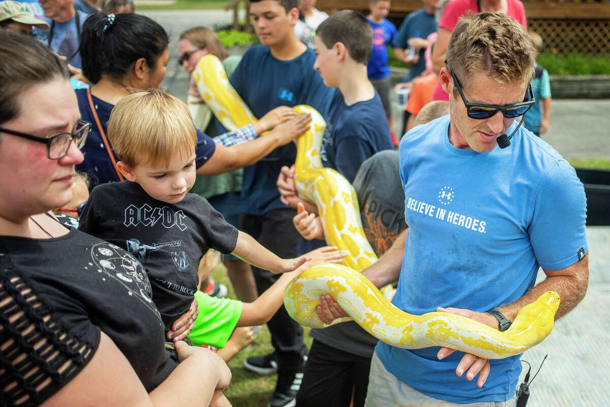 Tim Muxlow, owner of Muxlow Exotics, right, helps audience members hold and pet his 16-foot reticulated python after the first of three daily reptile and amphibian shows on Monday, Aug. 16, 2021 at the Midland County Fair. (Katy Kildee/kkildee@mdn.net)