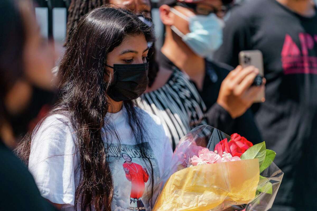 A woman holds a bouquet of flowers during a press conference at the site of Erik Salgado’s killing in Oakland.