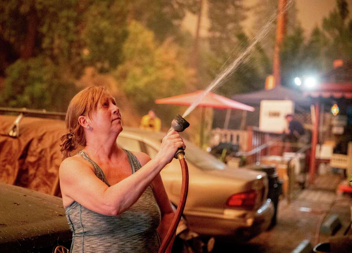 Jennifer Whitmore sprays her home with water as the Caldor Fire burns near White Hall, Calif., Tuesday, Aug. 17, 2021.
