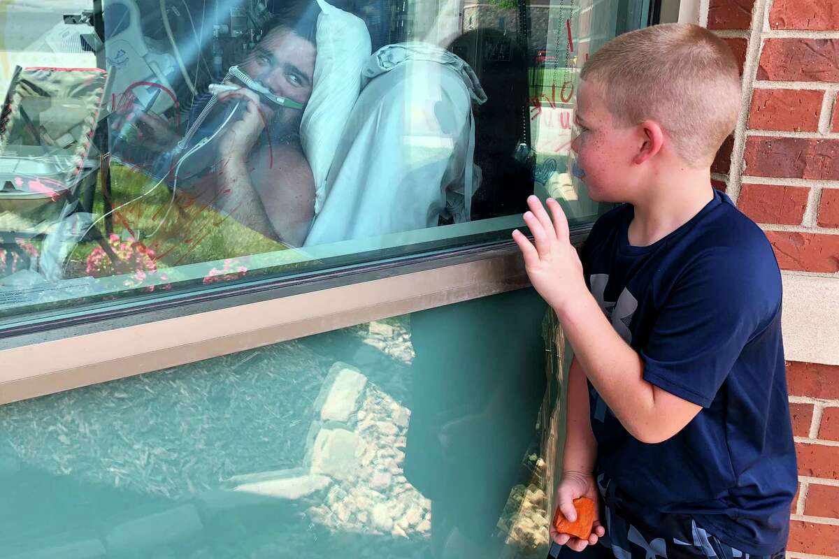 FILE - In this July 26, 2021, file photo, Brody Barker waves to his father, Daryl, from outside his hospital room in Osage Beach, Mo., as he recovers from COVID-19. Many overwhelmed hospitals, with no beds to offer, are transporting critically ill COVID-19 patients hundreds of miles to far-flung states for treatment. The delta variant of the virus, combined with low vaccination rates in many states, is causing a surge that has hospitals scrambling to find bed space.